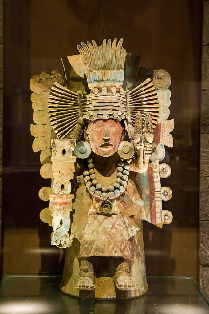 这位祭司,头戴华丽的羽毛,手上拿着两根玉米